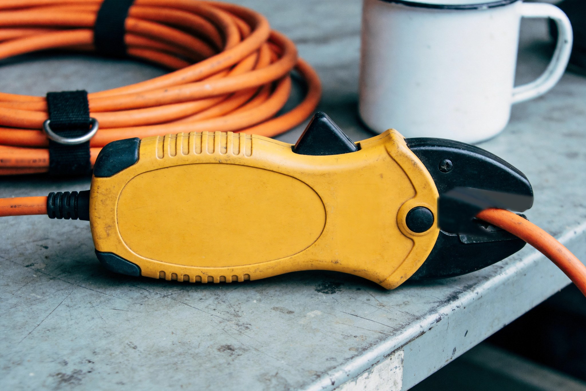 A clamp meter and an outlet tester on a workbench beside a coil of cord.